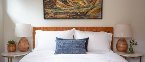 A hotel room with a large bed, two nightstands, a painting on the wall, and a window.