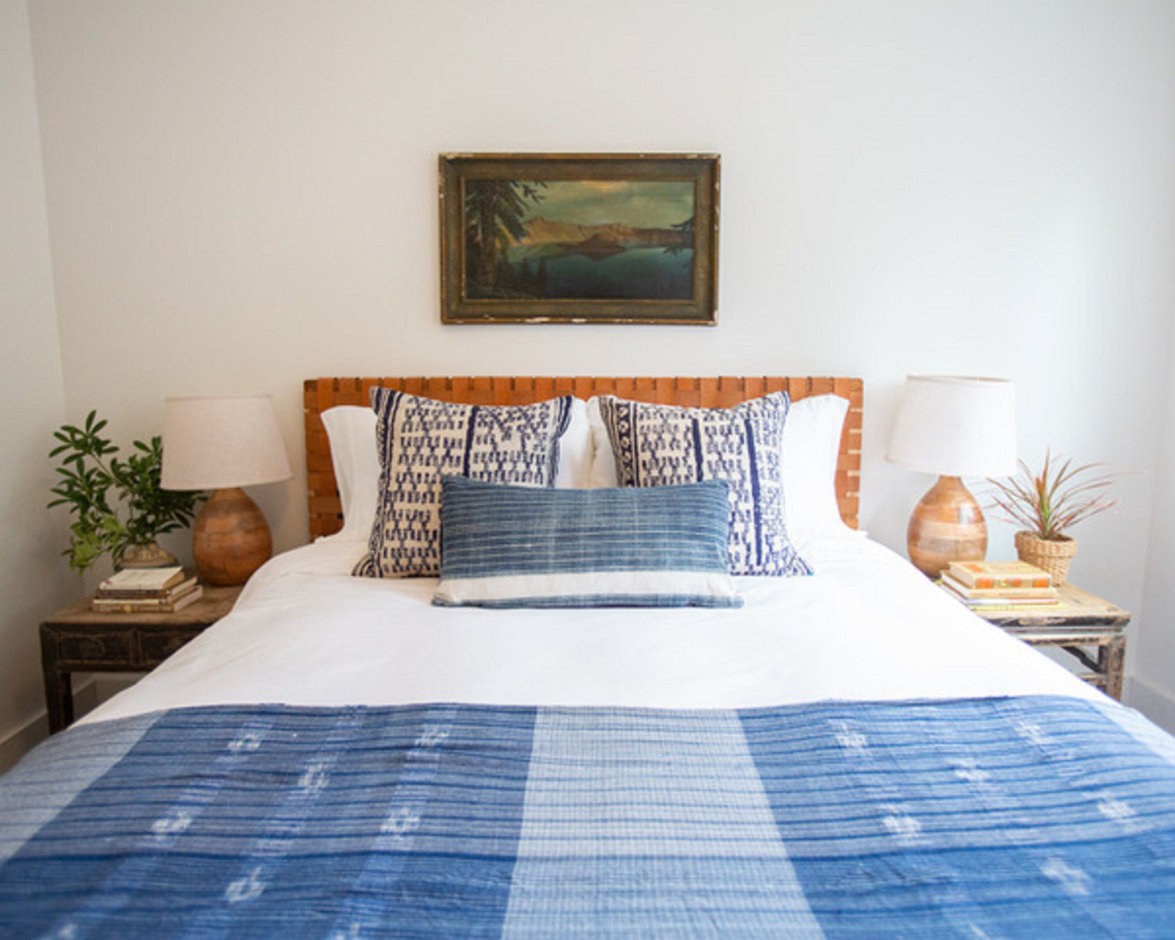 A neatly made bed with patterned pillows and a blue blanket, flanked by two bedside tables with lamps and books.
