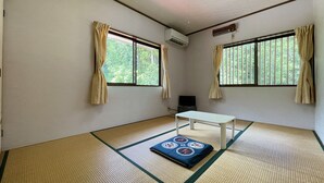 Een kamer met tatami vloermatten, een witte tafel en twee ramen met gordijnen.