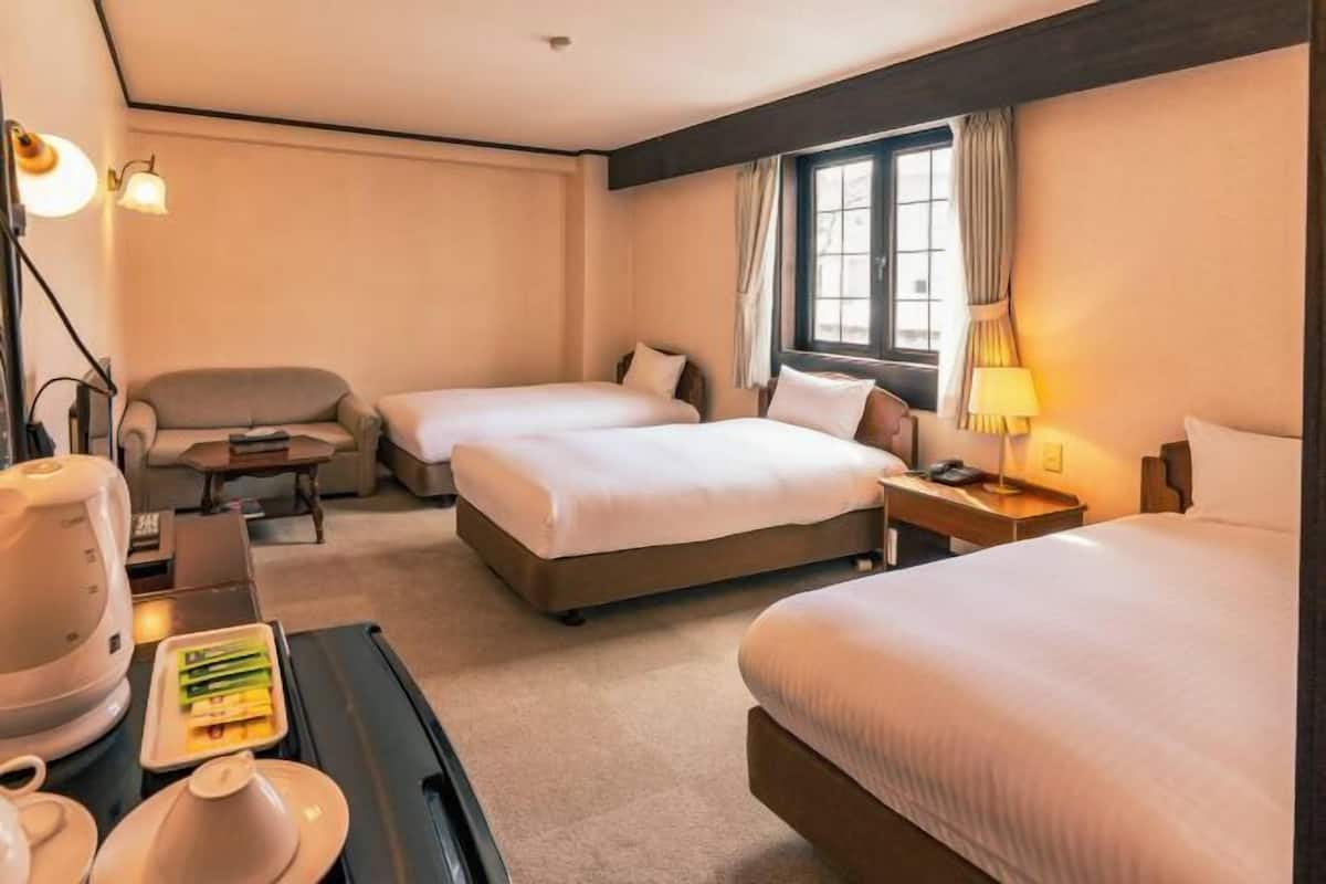 A hotel room with two beds, a desk with a lamp, a chair, and a coffee maker.