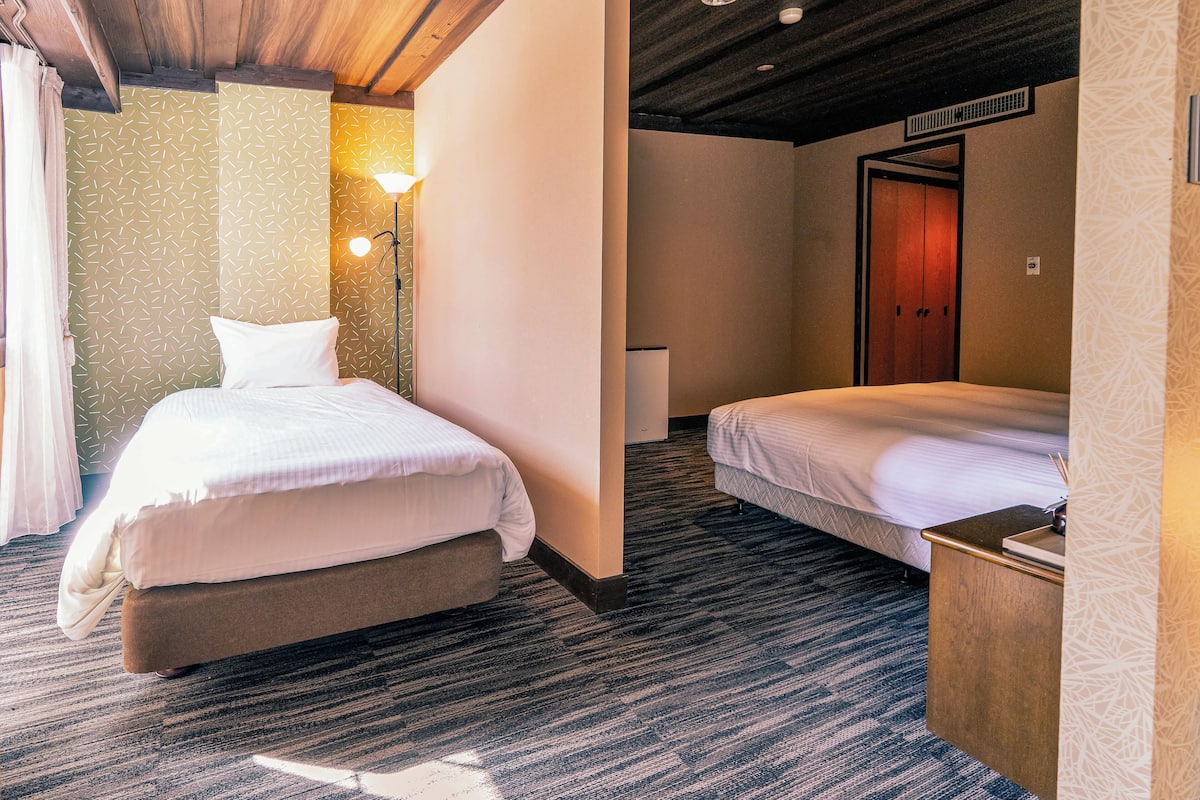 A hotel room with a bed, bedside table, lamp, and a door.