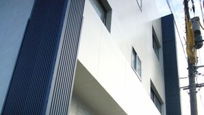 Un edificio moderno con fachada blanca, puerta de entrada de vidrio y una máquina expendedora en la acera.