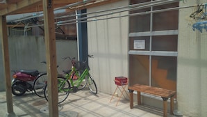 Un espacio exterior techado con una bicicleta, un patinete y un banco.