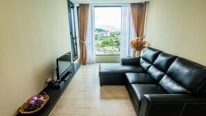 A modern living room with a black leather sofa, a flat-screen TV, and a view of a cityscape through large windows. - Marina Travellers Suite SKY Karamunsing (Kota Kinabalu)