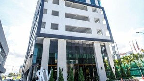 A modern high-rise building with a prominent 'KY' logo, large windows, and a landscaped entrance area. - Marina Travellers Suite SKY Karamunsing (Kota Kinabalu)