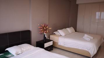 A hotel room with two beds, a nightstand with a vase of flowers, and a wardrobe.