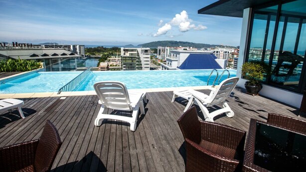 A rooftop pool with clear blue water, white lounge chairs, and a view of the cityscape and mountains in the background. - Marina Travellers Suite SKY Karamunsing (Kota Kinabalu)