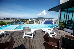 A rooftop pool with clear blue water, white lounge chairs, and a view of the cityscape and mountains in the background. - Marina Travellers Suite SKY Karamunsing (Kota Kinabalu)