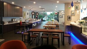 A restaurant with a long counter, multiple tables, and chairs. There are decorative lights and a view of the outside. - Marina Travellers Suite SKY Karamunsing (Kota Kinabalu)