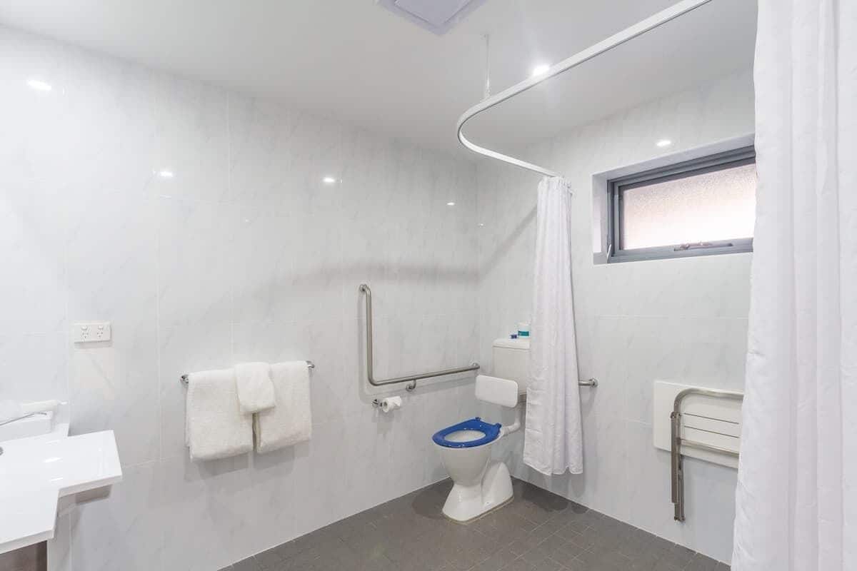A modern bathroom with a white sink, a toilet with a blue seat, a shower area, and a window.
