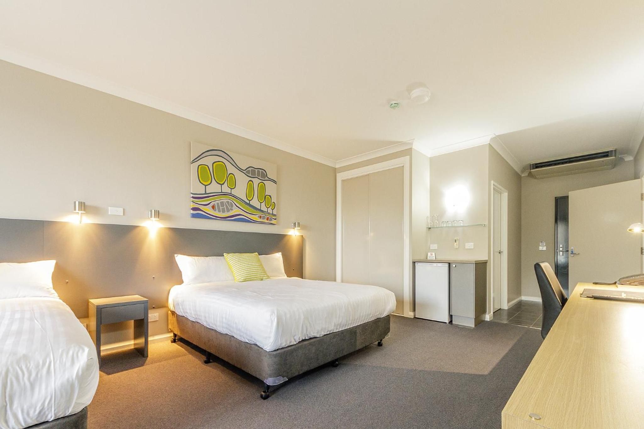 A hotel room with a bed, bedside tables, a desk, and a small kitchenette.