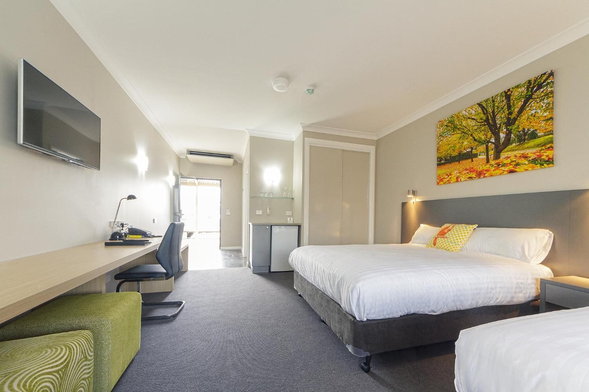 A hotel room with a bed, desk, chair, and a painting on the wall.