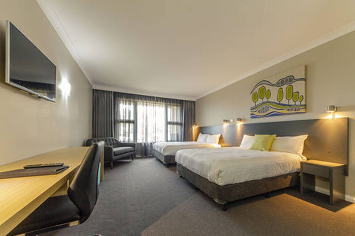 A hotel room with a bed, a desk, a chair, a TV, and a painting on the wall.