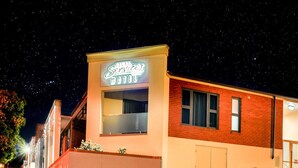 Un motel avec une enseigne au néon, une façade en briques et un ciel nocturne dégagé.
