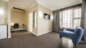 Une chambre d’hôtel équipée d’un bureau, d’une chaise, d’une télévision et d’une grande fenêtre avec des rideaux.