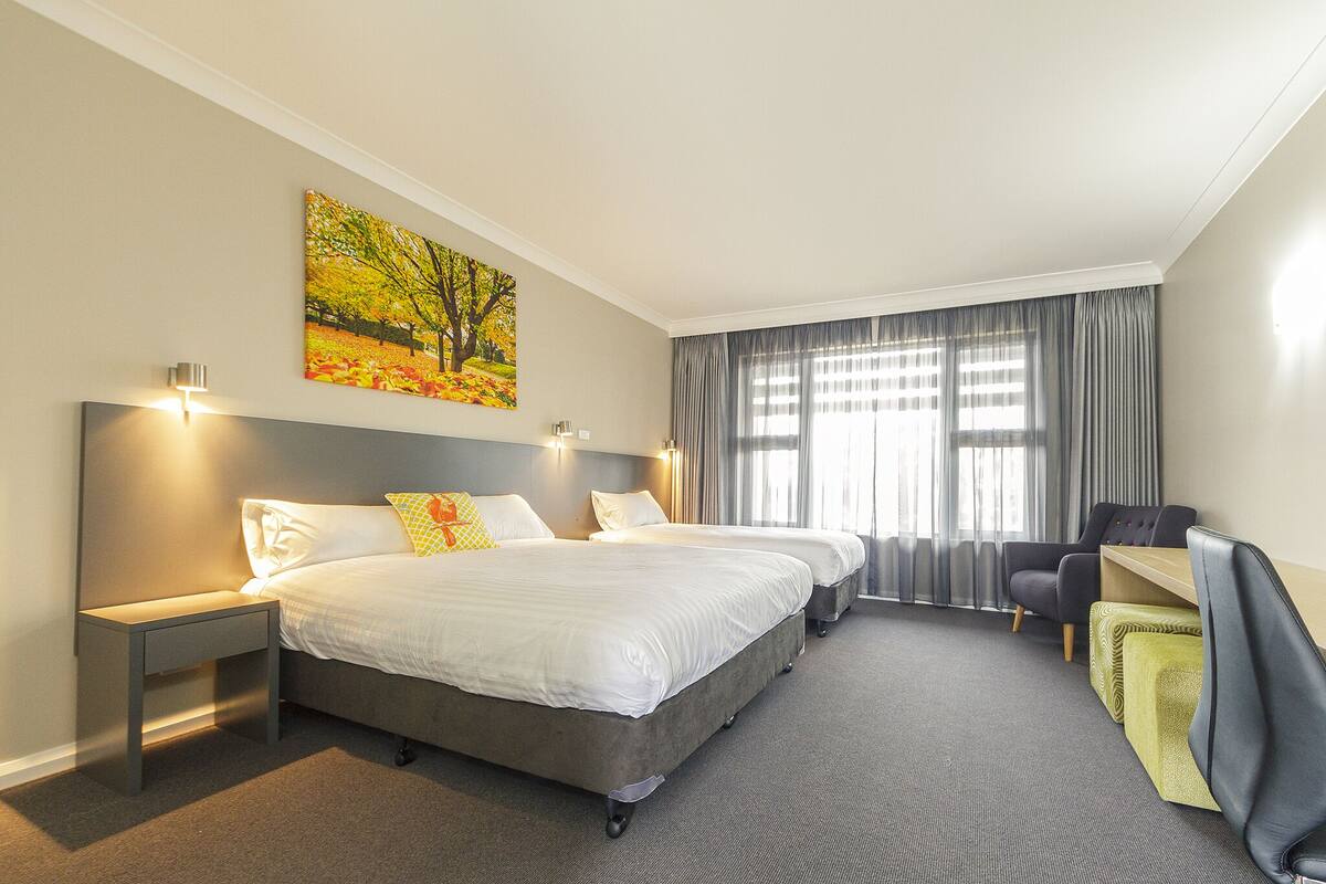 A hotel room with two beds, a desk, a chair, and a painting on the wall.