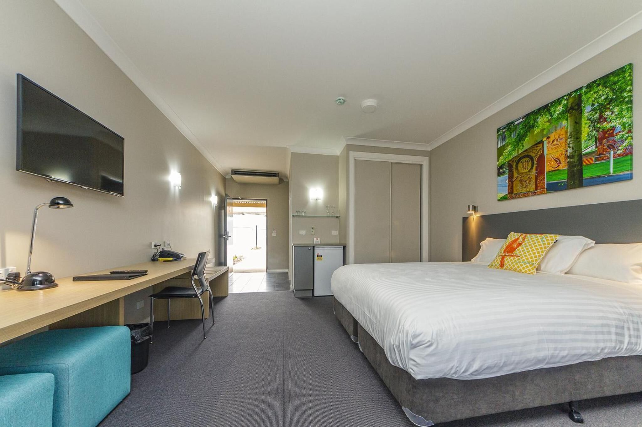 Habitación de hotel con cama, escritorio, silla, televisor y una obra de arte en la pared.