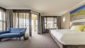 Une chambre d’hôtel avec un grand lit, un fauteuil bleu, une petite table et un tableau au mur.