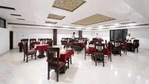 A spacious dining area with multiple tables and chairs, a clean and modern ceiling design, and a large window providing natural light. - Hotel East Gate (Agra)