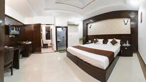 A modern hotel room with a large bed, a desk, a TV, and a bathroom with a shower and toilet. - Hotel East Gate (Agra)