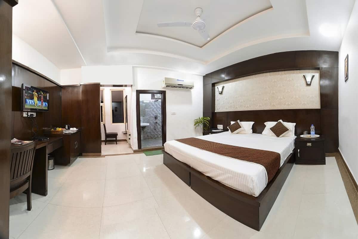 A modern hotel room with a large bed, a desk, a TV, and a bathroom with a shower and toilet.
