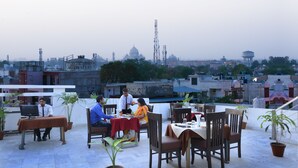 A rooftop dining area with tables and chairs, potted plants, and a cityscape view in the background. - Hotel East Gate (Agra)