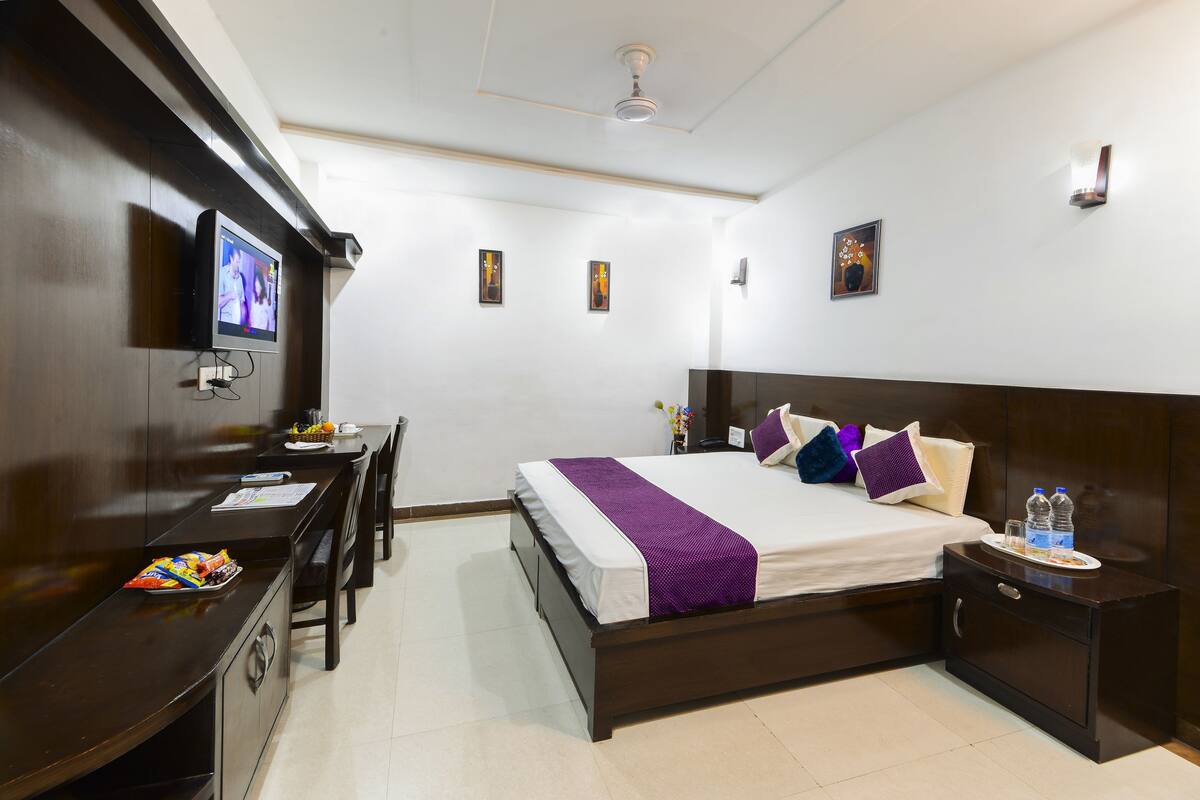A hotel room with a bed, bedside table, desk, chair, and a television on the wall.