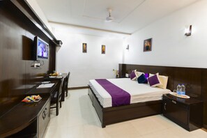 Una habitación de hotel con cama, mesita de noche, escritorio, silla y televisión en la pared.