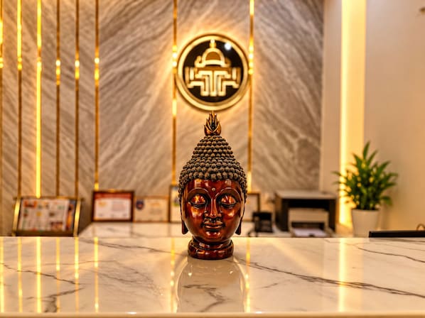 A Buddha statue on a marble surface with a patterned wall and a circular emblem in the background. - Hotel Taj Heights (Agra)