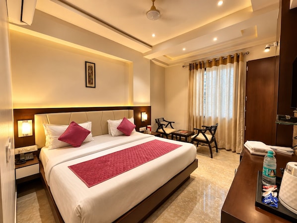 A hotel room with a bed, bedside tables, a desk, a chair, a television, and a bathroom. - Hotel Taj Heights (Agra)