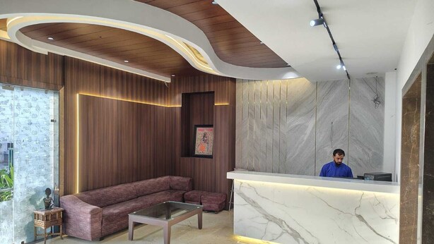 A modern reception area with a marble reception desk, a wooden ceiling, and a sectional sofa. - Hotel Taj Heights (Agra)