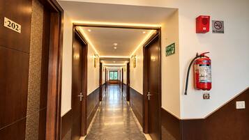 A hotel corridor with doors numbered 202, fire exit signs, a fire alarm, and a fire extinguisher.