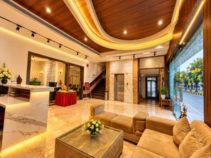 Un vestíbulo de hotel con mostrador de recepción, zona de estar y una escalera que lleva a los pisos superiores.