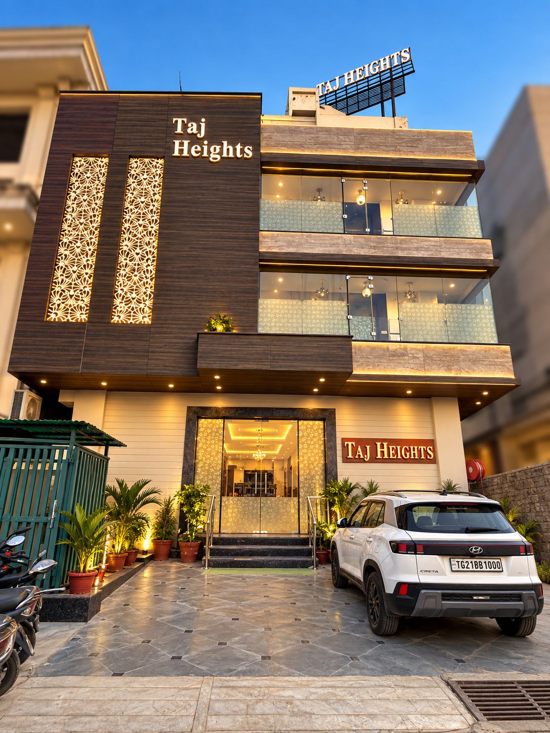 A modern building with a sign reading 'Taj Heights' and a white car parked in front.