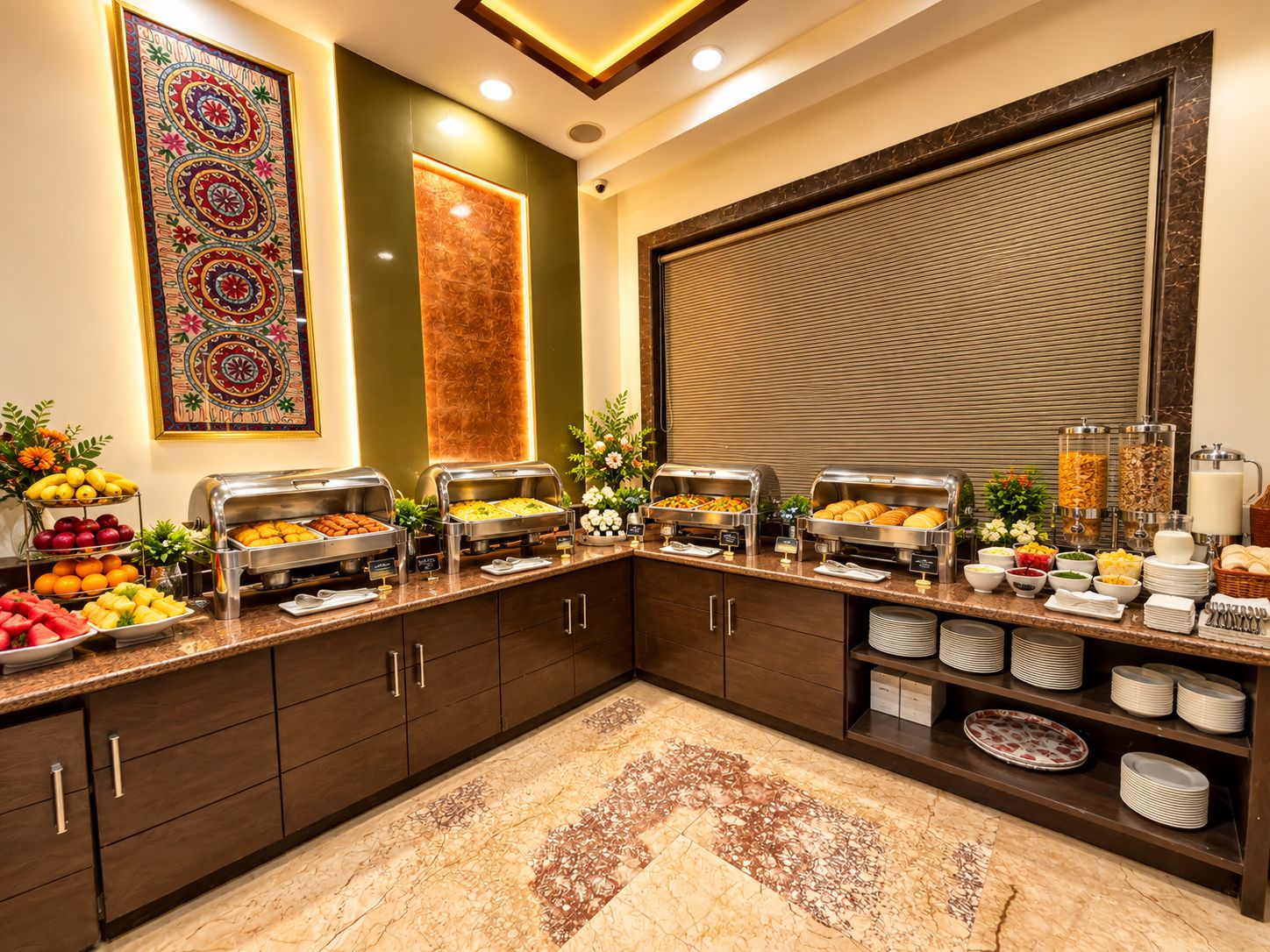 A buffet setup with various food items, a decorative wall piece, and a large window with blinds.