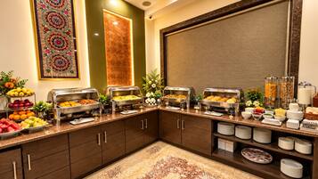 A buffet setup with various food items, a decorative wall piece, and a large window with blinds.