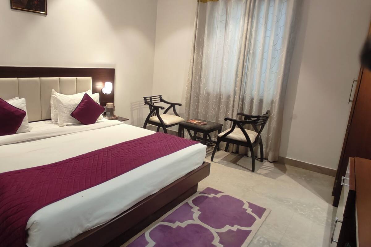 Une chambre d’hôtel avec un grand lit, deux tables de chevet, un bureau avec des chaises et une fenêtre avec des rideaux.