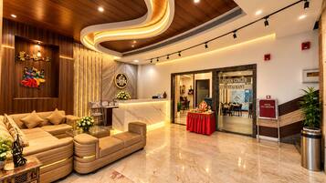 A hotel lobby with a reception desk, a sofa, a dining area, and a staircase.