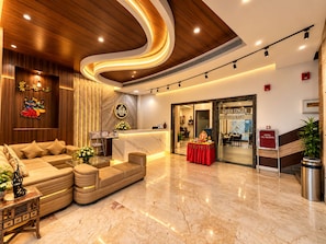 Un vestíbulo de hotel con mostrador de recepción, un sofá, un área de comedor y una escalera.