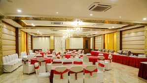 A banquet hall with rows of white chairs with red sashes, a buffet table, and a chandelier. - Hotel Taj Heights (Agra)