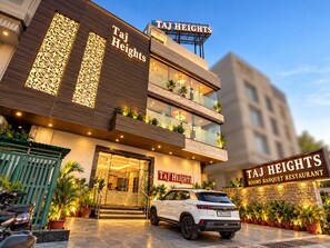 Un edificio moderno con un cartel que indica 'Taj Heights' y 'Salas de banquetes Restaurante'.