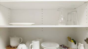 A white shelf with various white ceramic items including a teapot, cups, and a glass bowl.