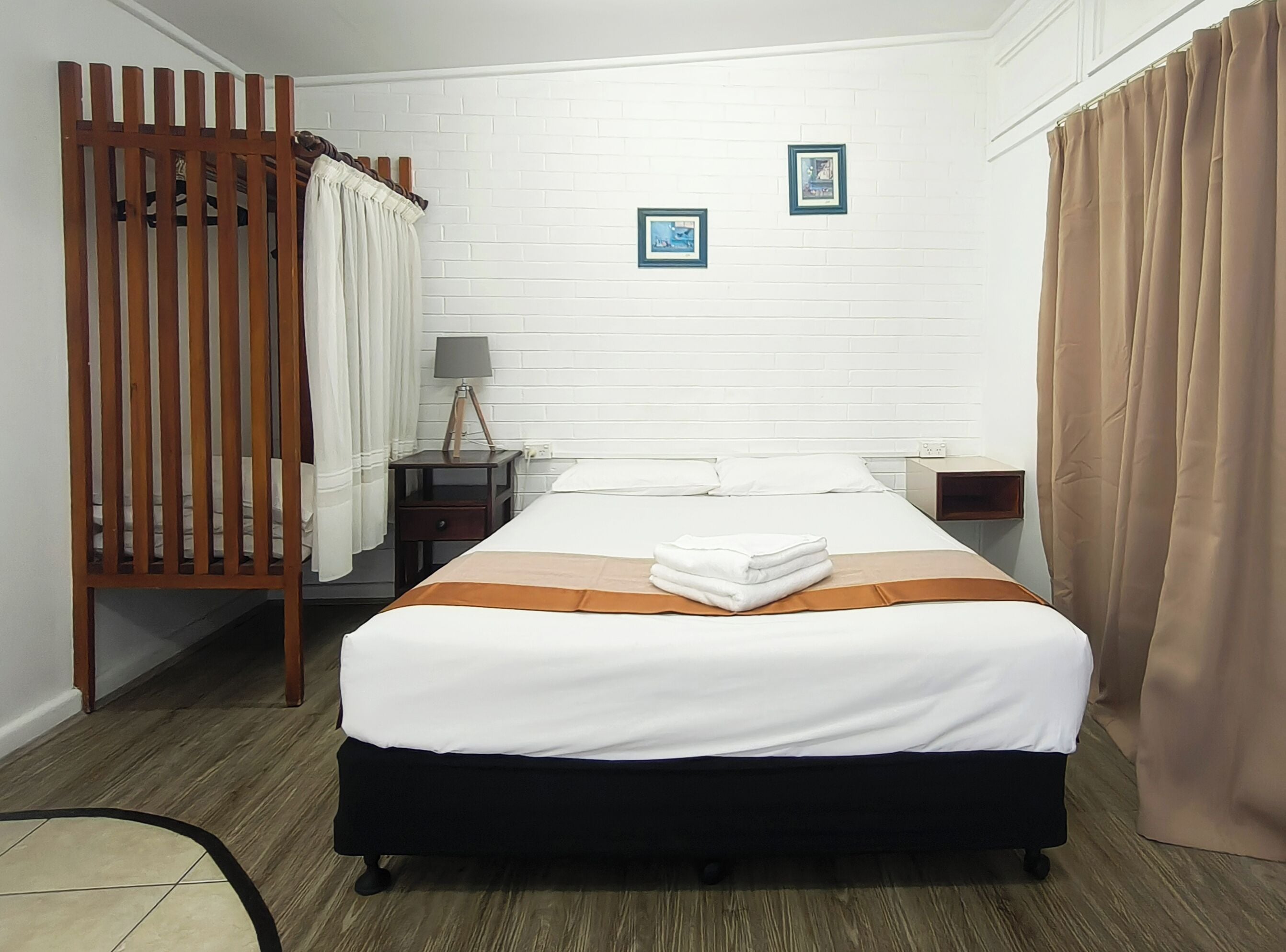 A hotel room with a bed, a wooden partition, a nightstand, a lamp, and two framed pictures on the wall.