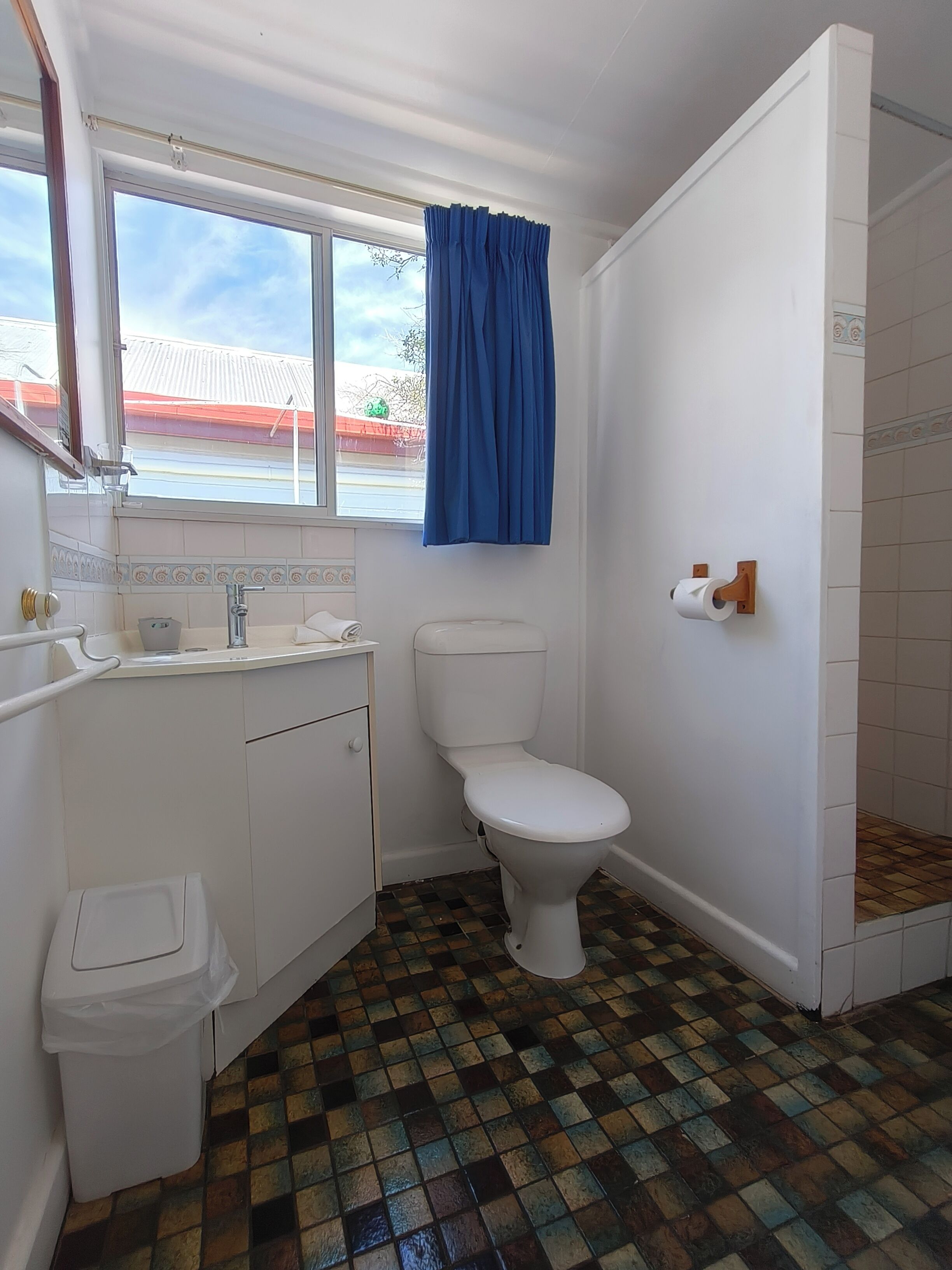 Un baño con inodoro, lavamanos y ventana con cortina azul.