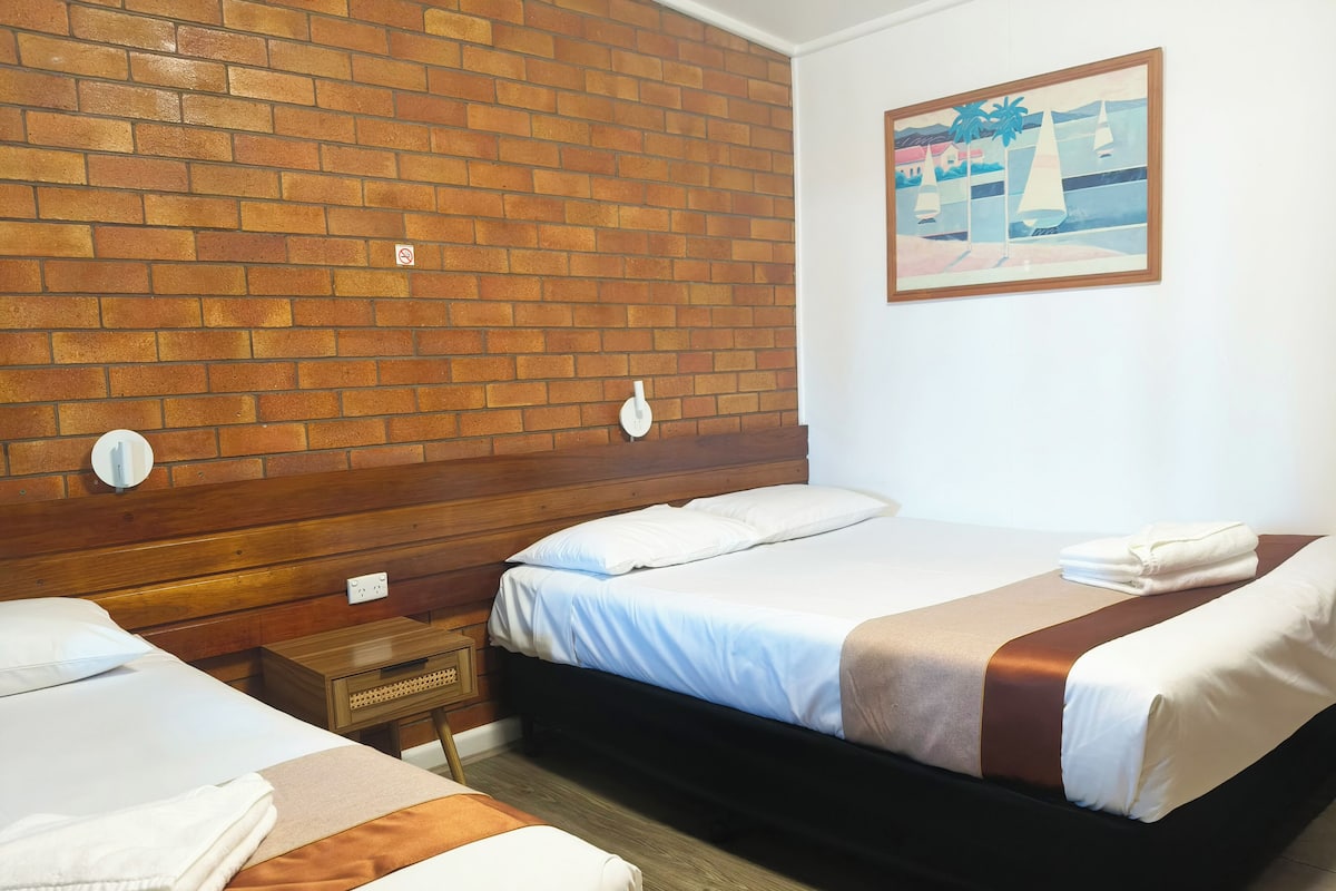A hotel room with a brick wall, two beds, a painting, and a wooden headboard.