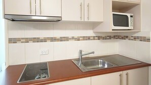 A kitchen with white cabinets, a stainless steel sink, and a microwave. - Motel Myall (Dalby)