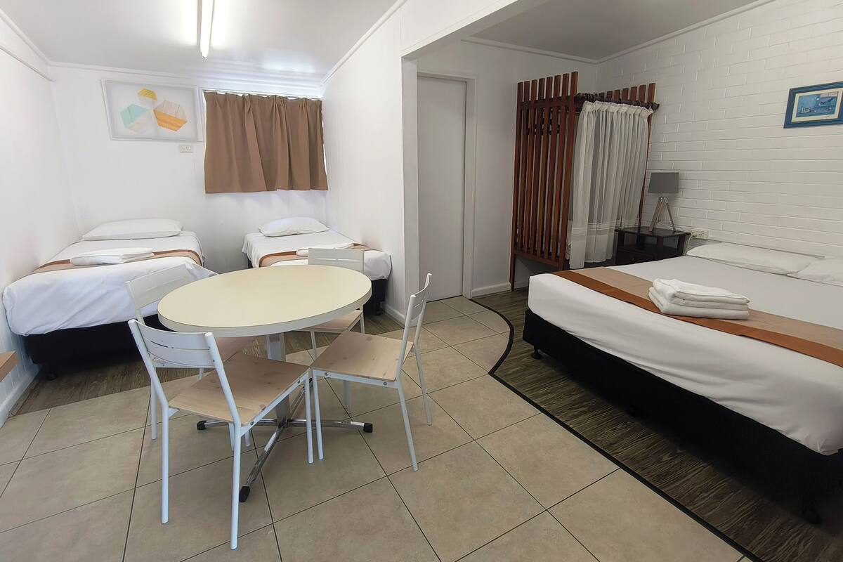 A hotel room with two single beds, a round table with chairs, a small desk, and a wardrobe.