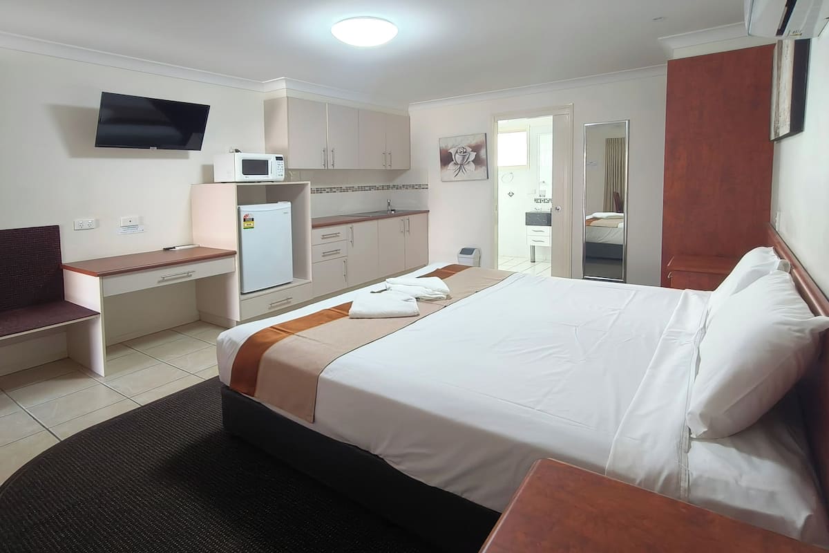 A hotel room with a bed, a desk, a microwave, a TV, and a bathroom visible through an open door.