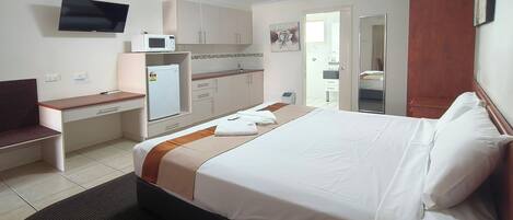 Habitación de hotel con cama, escritorio, microondas, televisor y baño a la vista a través de una puerta abierta.