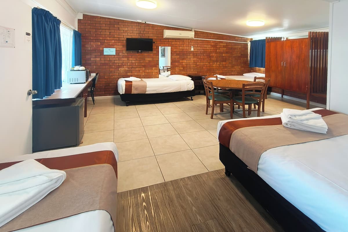 A hotel room with two beds, a dining table, chairs, a TV, and a brick wall.